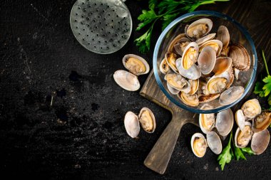 Fresh vongole in the bowl on a cutting board with parsley. On a black background. High quality photo