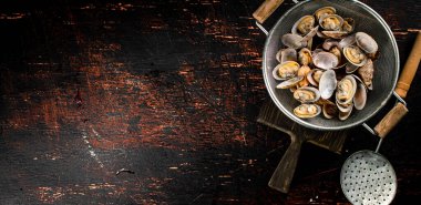 Vongole in a colander on a cutting board. On a rustic dark background. High quality photo