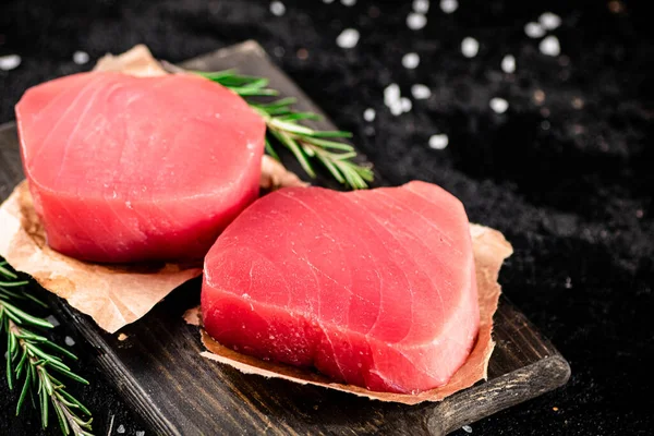 stock image Raw tuna steaks on a rosemary cutting board. On a black background. High quality photo