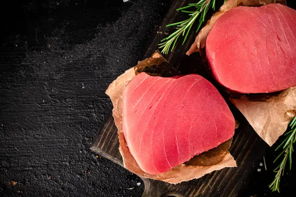 stock image Raw tuna steaks on a rosemary cutting board. On a black background. High quality photo