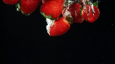 Çilekler kabarcıklarla suya düşer. Film, yavaş çekim 1000 fp. Yüksek kaliteli FullHD görüntüler