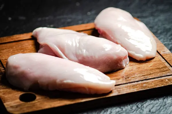 Fresh chicken fillet . On a black table.