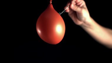 Dinamik bir video, kırmızı bir balonu şişiren, su sıçratan ve kırmızı bir objeyi siyah bir arka planda su sıçratan bir insanın renkli yakın plan çekimleri sergiliyor.