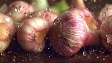 Sarımsak, doğal gıdaların bir bileşeni, ahşap bir masada suyla yıkılıyor. Allium cinsinde bir karasal bitki olan bu sebze, morumsu çiçekli olayıyla bilinir.