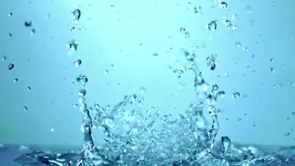 透明なガラスの表面に飛び散る水滴のクローズアップショットは 空の背景に対する魅惑的な電気ブルー効果を作成します — ストック動画