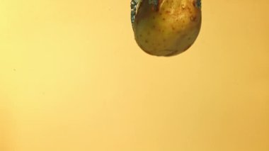 Süper yavaş çekim patatesleri sarı arka planda suyun altına düşer. Yüksek kaliteli FullHD görüntüler