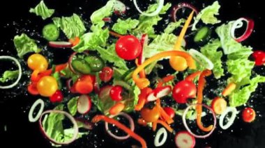 Marul, domates, biber, soğan ve diğer sebzelerden yapılmış taze bir salata. Hepsi de doğal renklerini ve dokularını vurgulamak için parlak siyah bir arka planda sergileniyor.