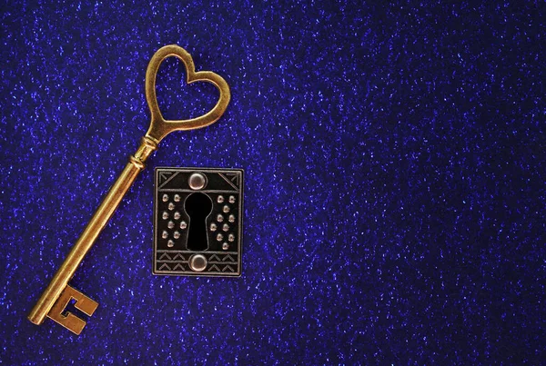 古色古香的金钥匙 心形顶部 华丽的锁在闪闪发光的蓝底上 图库图片