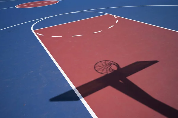 空旷的蓝色户外篮球场 网子和背板在阴影中 免版税图库照片