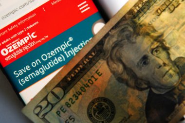 Raleigh, NC - ABD - 08-15-2024: Ekranda Ozempic web sitesi olan bir cep telefonu ve 20 dolarlık bir fatura