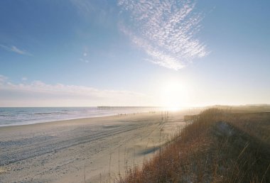İnsanlar Sunset Beach North Carolina 'daki rıhtımın yakınındaki sahilde.                               