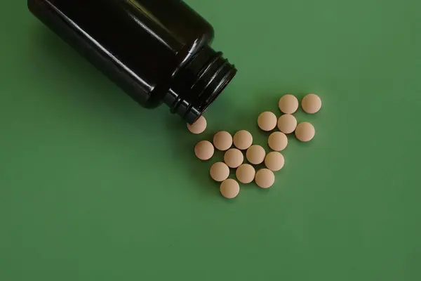 Stock image pills with container against green background