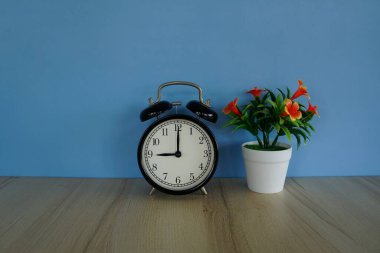 Çiçek saksısı ve çalar saat masanın üstünde.