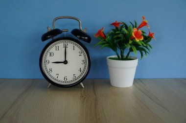 Çiçek saksısı ve çalar saat masanın üstünde.