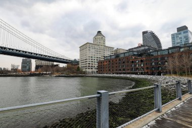 Brooklyns DUMBO 'dan Manhattan Köprüsü manzaralı bir kar yağışı. Karla kaplı sokaklar, rıhtım ve ikonik köprü yapısı Manhattan ufuk çizgisine karşı sakin bir kış manzarası yaratıyor..