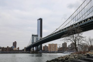 Brooklyns DUMBO 'dan Manhattan Köprüsü manzaralı bir kar yağışı. Karla kaplı sokaklar, rıhtım ve ikonik köprü yapısı Manhattan ufuk çizgisine karşı sakin bir kış manzarası yaratıyor..