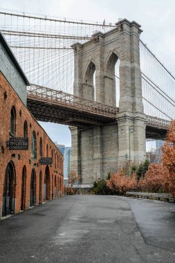 Brooklyn, NYC 'deki DUMBO mahallesinden Brooklyn Köprüsü' nün manzarası. Doğu Nehri boyunca uzanan tarihi asma köprü, arka planda parke taşı karlı sokaklar, rıhtım ve ikonik Manhattan silueti tarafından çerçevelenmiştir..