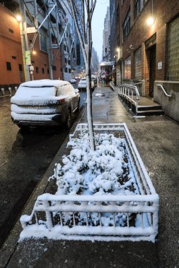 Kışın hareketli bir New York sokak sahnesi, karla kaplı sokaklar, yayalar paltoya sarılı, sarı taksiler, ve yüksek gökdelenler. Sahne, Manhattan 'ın canlı enerjisini soğuk, şenlikli ve kış atmosferinin ortasında yakalıyor..
