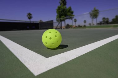 Tight focus on a pickleball on a court with white lines. The sport of pickleball has become the fastest growing sport in America. clipart