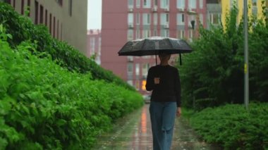 Şemsiyeli bir kadın yağmurun altında yürüyor. Yağmurlu bir yaz günü, elinde şemsiyeyle ıslak yolda yürüyen bir kız. Yavaş çekim. Yüksek kalite 4k görüntü