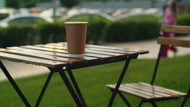 紙コーヒーカップに降る雨が降る 雨の下にオープンテラスの木製テーブル 夏の雨の中のストリートカフェ スローモーション — ストック動画
