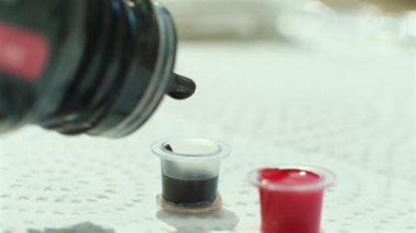 Dövme ustası dövme için boya alır. Dövme için kırmızı ve siyah mürekkeple doldurulmuş iki şapka. Dövme mürekkebi yakın planda düşer.