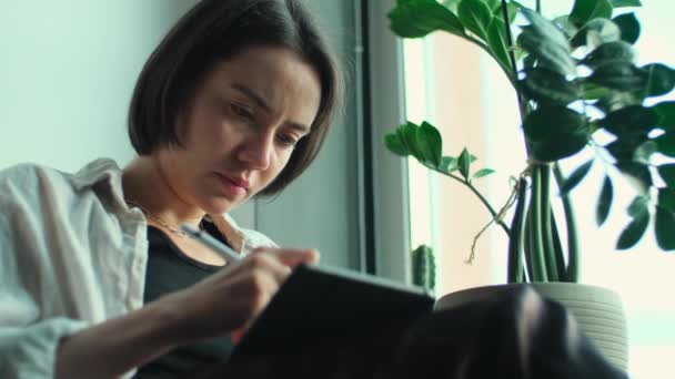 デジタルタブレットで描いた女性アーティスト デジタル鉛筆を手に持ったクリエイティブな少女が自宅から遠隔操作 コンピュータを使用して 窓の近くに座っているアートを作成するフリーランサー — ストック動画