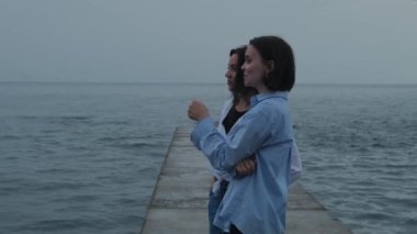 Dalgakıranın üzerinde duran ve deniz ufkuna bakan iki kız. Kız arkadaşlar sakin dalgalarla deniz manzarası seyredip sohbet ediyorlar. Yüksek kalite 4k görüntü