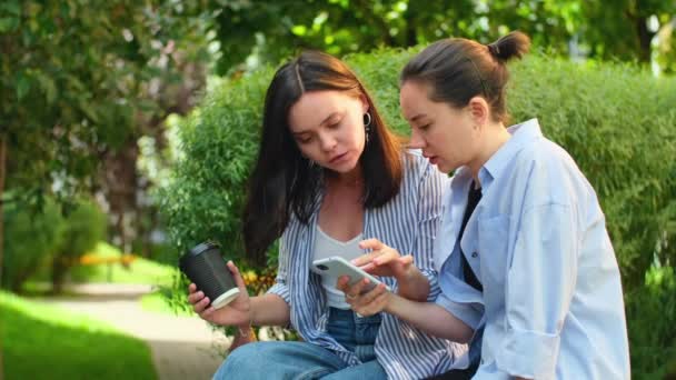 Dwie Kobiety Patrzące Telefon Komórkowy Zewnątrz Przyjaciółki Przewijają Smartfona Siedząc — Wideo stockowe