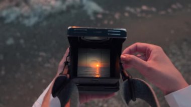 Eski film kamera görüntüleyicisinden bak. Dişi eller, geriye dönük analog tr orta formatta 120 mm 'lik kamera tutuyor ve gün batımında sahilde denizin fotoğrafını çekiyor. Yüksek kalite 4k görüntü.