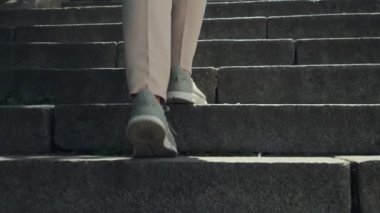 Merdivenlerden çıkan bir kadın. Güneşli bir günde şehirde taş merdivenlerden çıkan spor ayakkabılı kadın bacakları. Arkaya yakın bir görünüm. Yüksek kalite 4k görüntü