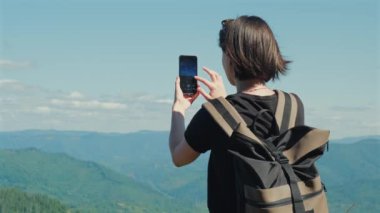 Kadın gezgin cep telefonuyla dağ manzarasının fotoğraflarını çekiyor. Sırt çantalı bayan otostopçu seyahat blogcusu dışarıda sosyal medya için içerik yaratıyor. Yüksek kalite 4k görüntü