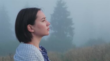 Genç bayan dışarıda derin nefes alıyor. Dağlarda sisli bir sabahta güzel, rahat bir kız portresi. Sinematik çekim. Yüksek kalite 4k görüntü