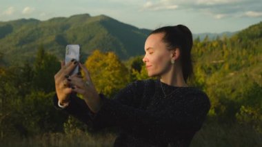 Dağ zirvesinde cep telefonu kullanarak selfie çeken genç bir kadın. Mutlu kız cep telefonu kamerasıyla sosyal medya için fotoğraf çekiyor, manzara manzaralı. Yüksek kalite 4k görüntü