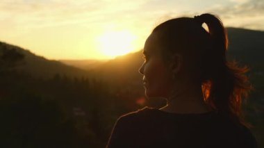 Genç bir kadın dağlarda günbatımının tadını çıkarıyor. Güzel kadın yürüyüşçü portresi dağların eteklerindeki vadi manzarasına, dikiz manzarasına bakıyor. Yüksek kalite 4k görüntü