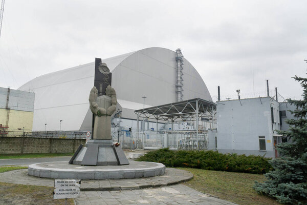 Памятник ликвидаторам с атомной Чернобыльской установкой позади них и 4-й контейнер с ядерным радиационным реактором в пасмурный день