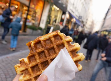 Arka planda bulanık efektli brusselas sokaklı Belçika ısırık waffle 'ını tutan bir erkeğin ilk görüntüsü