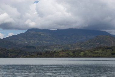 Güneşli bir günde göl kıyısından görünen bulutlarla dolu güzel And Dağları.