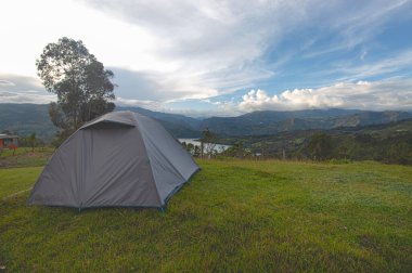 Güneşli bir öğleden sonra, arka planda göllü ve dağlı yeşil bir çim dağının üzerinde çadır kurmak.
