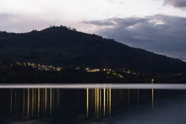 stock image Beautiful Colombian Gachala town landscape with night light refflected on guavio reservoir lake and a big mountain silhouette on violet sunset