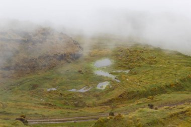 a small swamp system at colombian paramo cloudy landscape near to a sand road