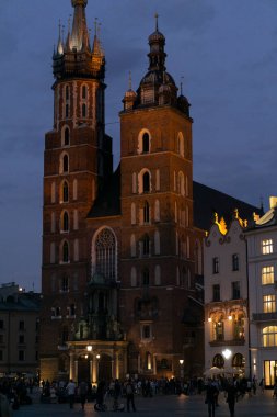 Akşam karanlığında turistlerle dolu Krakow Meydanı. Arka planda Aziz Mary Bazilikası var.