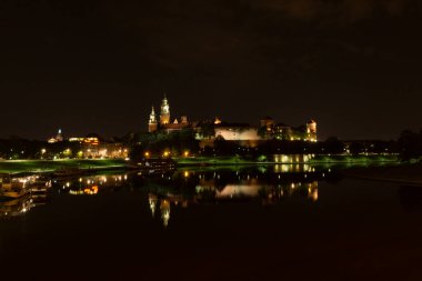 Krakow şehri gece manzarası Wavel kalesi ve Vistula nehri olan bir köprüden görülüyor.