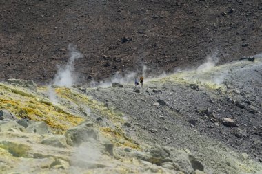 Bir çift turist, aktif bir volkanın ve fümerollerin ortasında güneşli bir günde yürüyüş yoluna doğru yürür.
