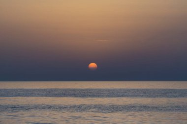 Bulutsuz ve sakin denizsiz turuncu yuvarlak güneşin güzel alacakaranlık sahnesi