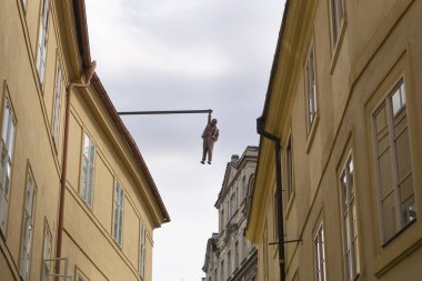 Sigmund Fred Heykel, Prag şehir binalarının ortasında bir sopaya tutunuyor.