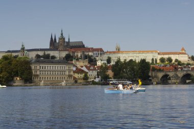 Güneşli günbatımında Prag kalesi ve turistik binalarla Vltava nehrinde seyahat eden turist.