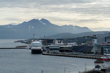 Arka planda büyük bir gemi demirli ve dağları tütsüleyen Tromso limanı
