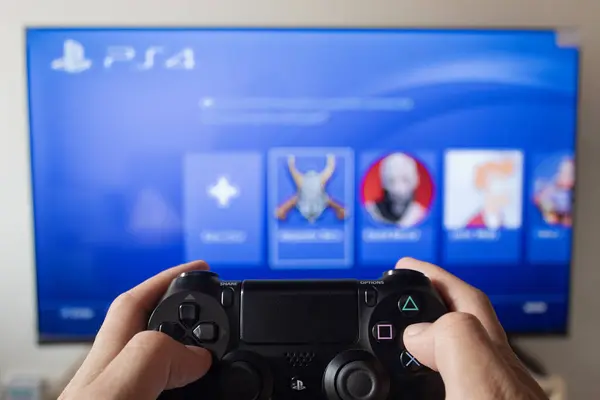 stock image A male hand holding a play station 4 controller with play station 4 interface in a smart tv at background