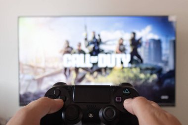 Arka planda Warzone Call of Duty nişancısı giriş video oyunu olan bir erkek el, oyun istasyonu 4 kontrolörü tutuyor.